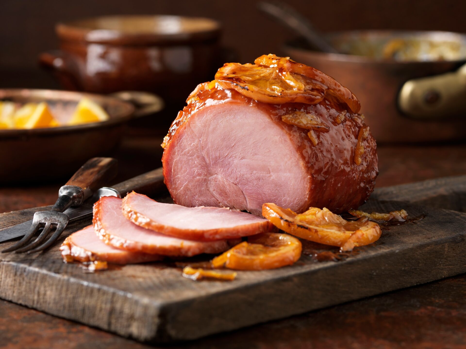 roast gammon with apricot glaze and orange slices on a dark wood chopping board