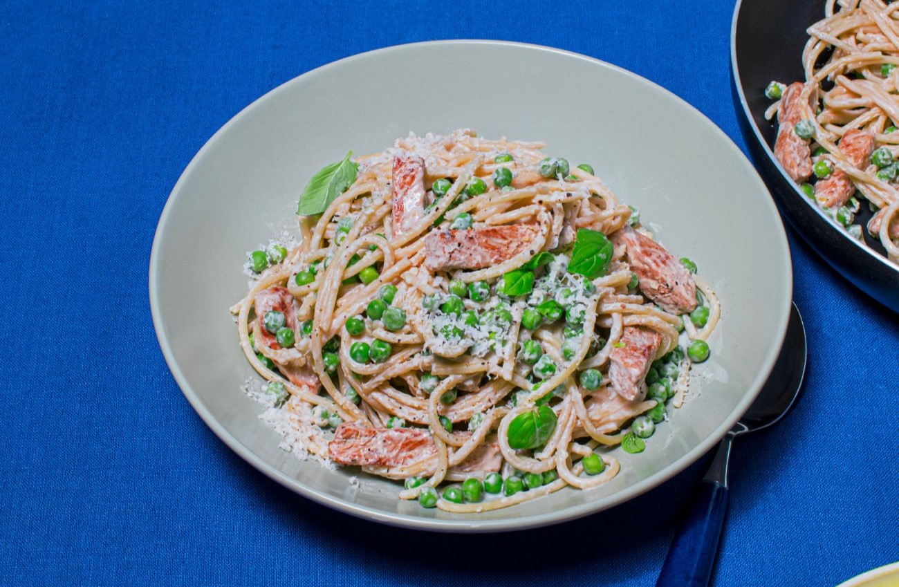 Creamy Lemon Pork Pasta with Peas in a nude bowl with blue backdrop.