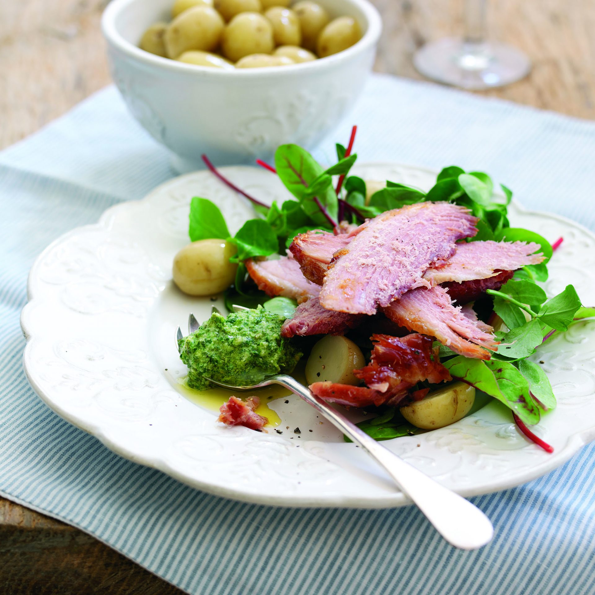 Slices of baked ham served on top of a fresh salad, on a white plate