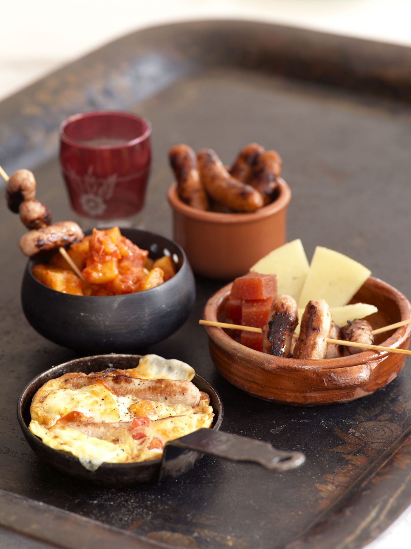 Mini pots filled with tapas items including patatas bravas and mini sausage skewers