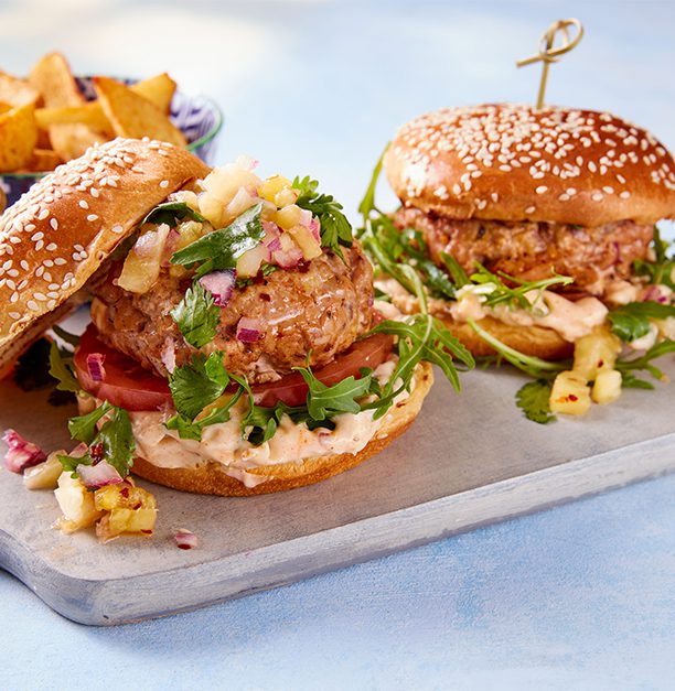 Two burger buns filled with a pork burger and pineapple salsa, on a board.