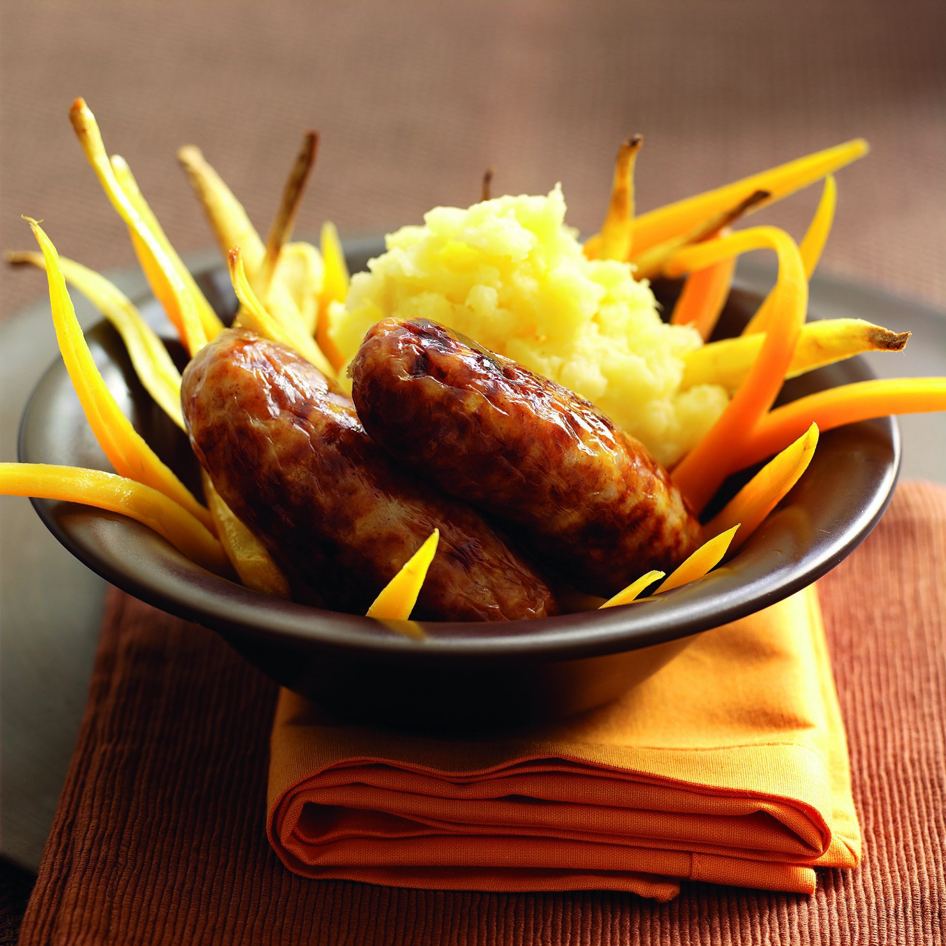 Two pork and apple sausages served in a black bowl with parsnip and potato mash