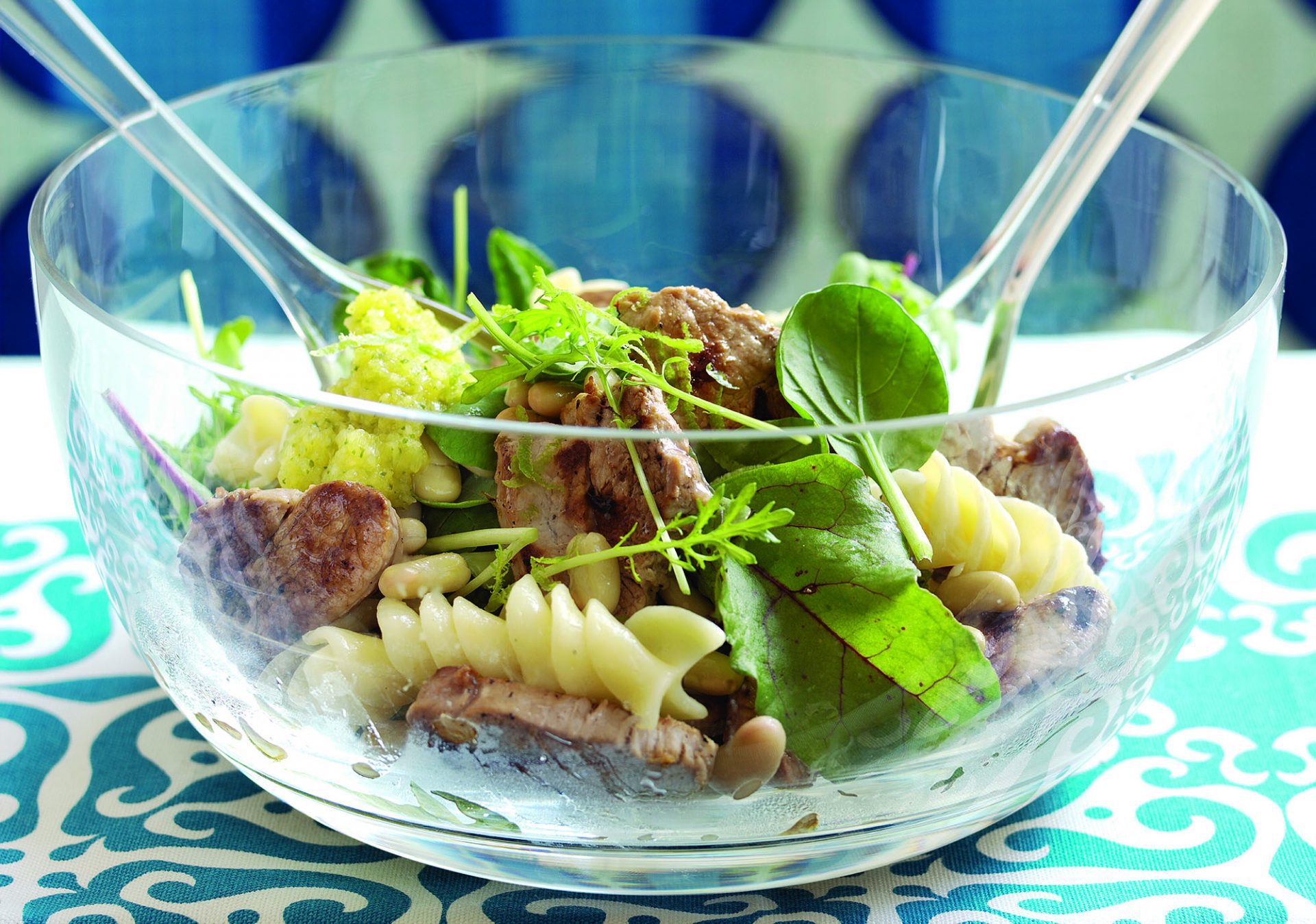 Pork pasta salad in a perspex salad bowl with serving spoon