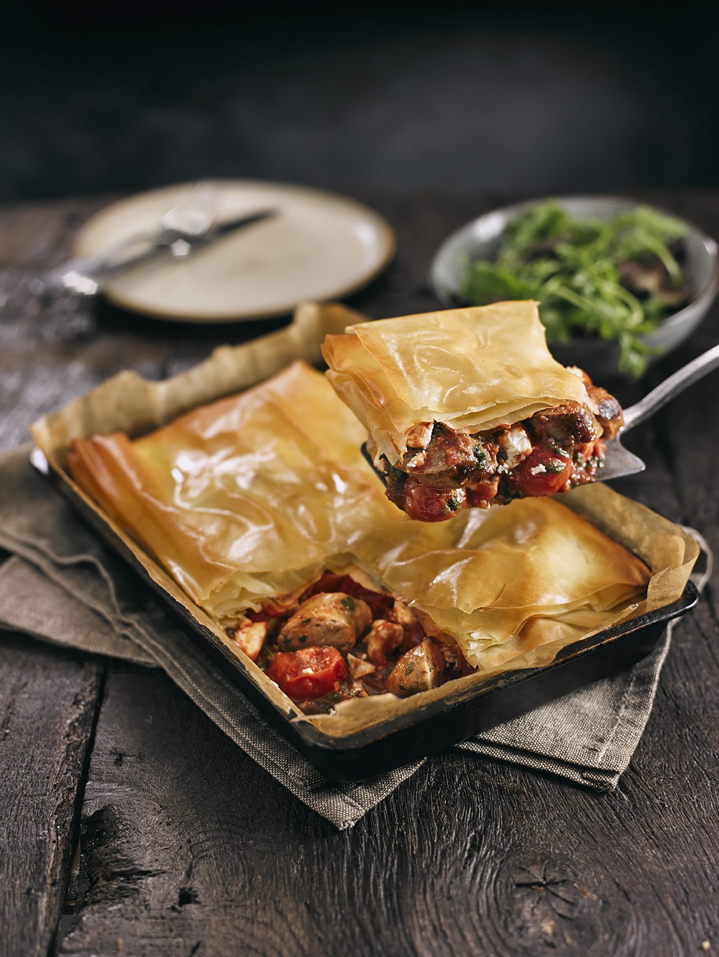 Sausage and feta pie with filo pastry top served in a black tray, single portion being spooned out