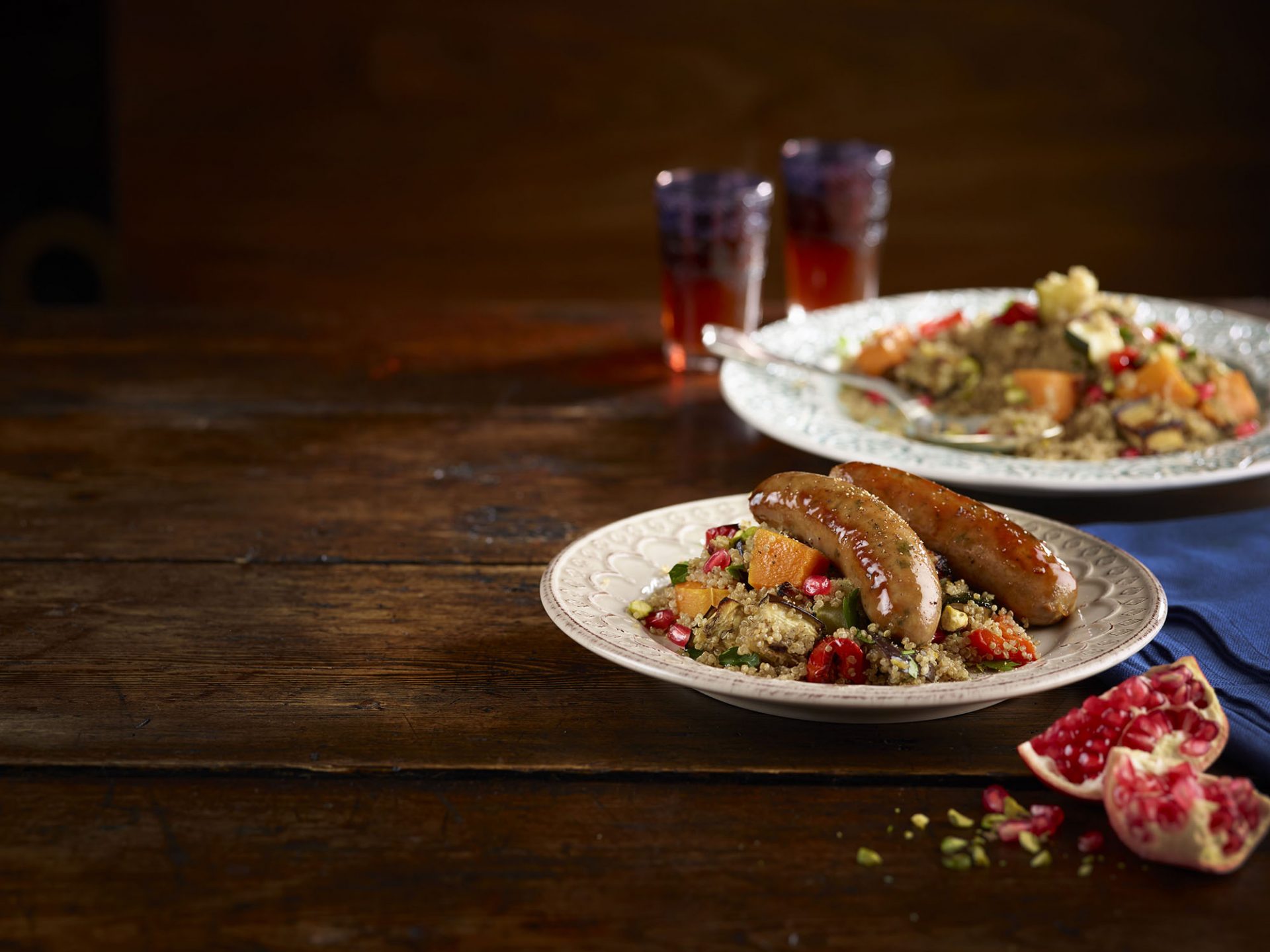 White plate with sausages on a bed of moroccan quinoa salad