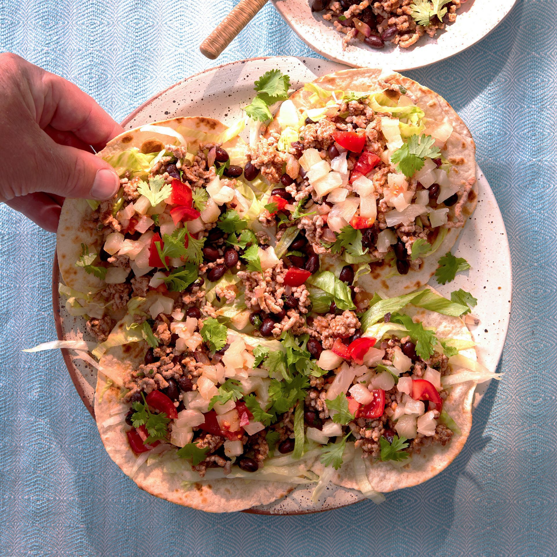 Four mini tostadas topped with pork mince and vegetables, hand grabbing one of the plate