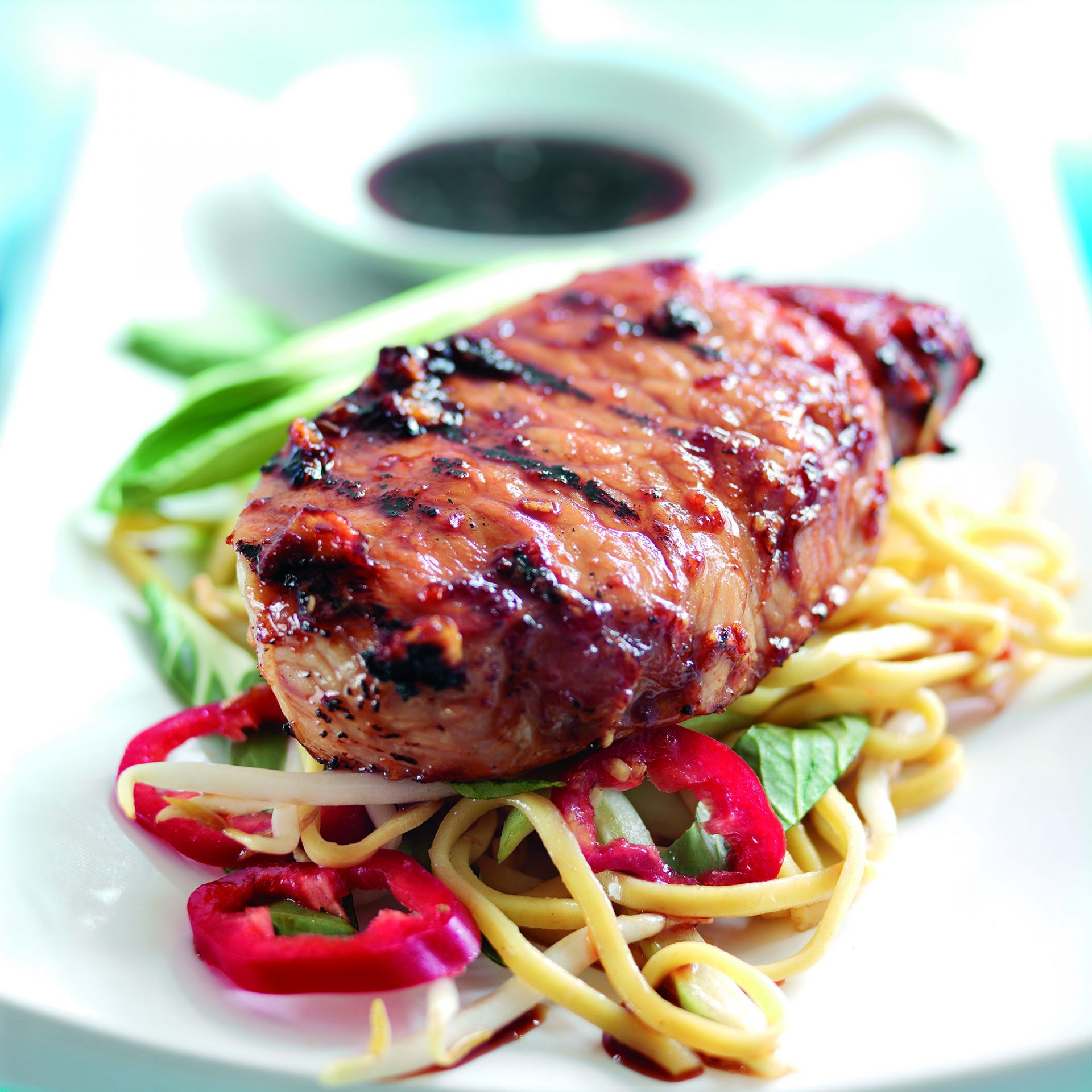 Teriyaki pork steak served on top of noodles and vegetables, on a white plate