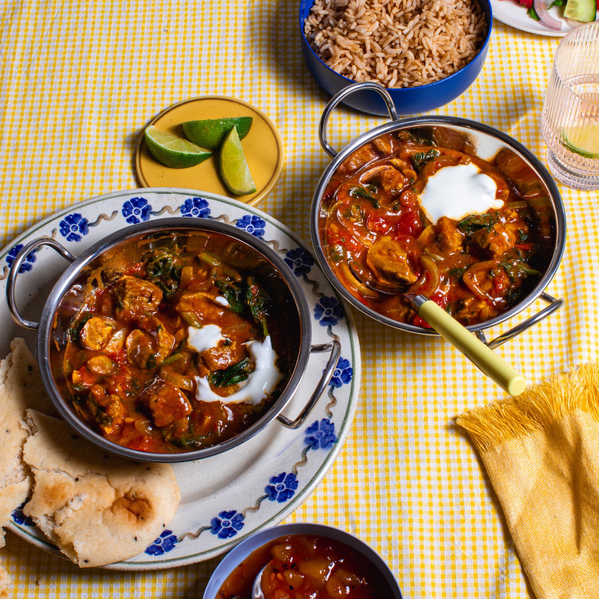 Pork madras curry served in dishes with rice and chutney on a yellow background