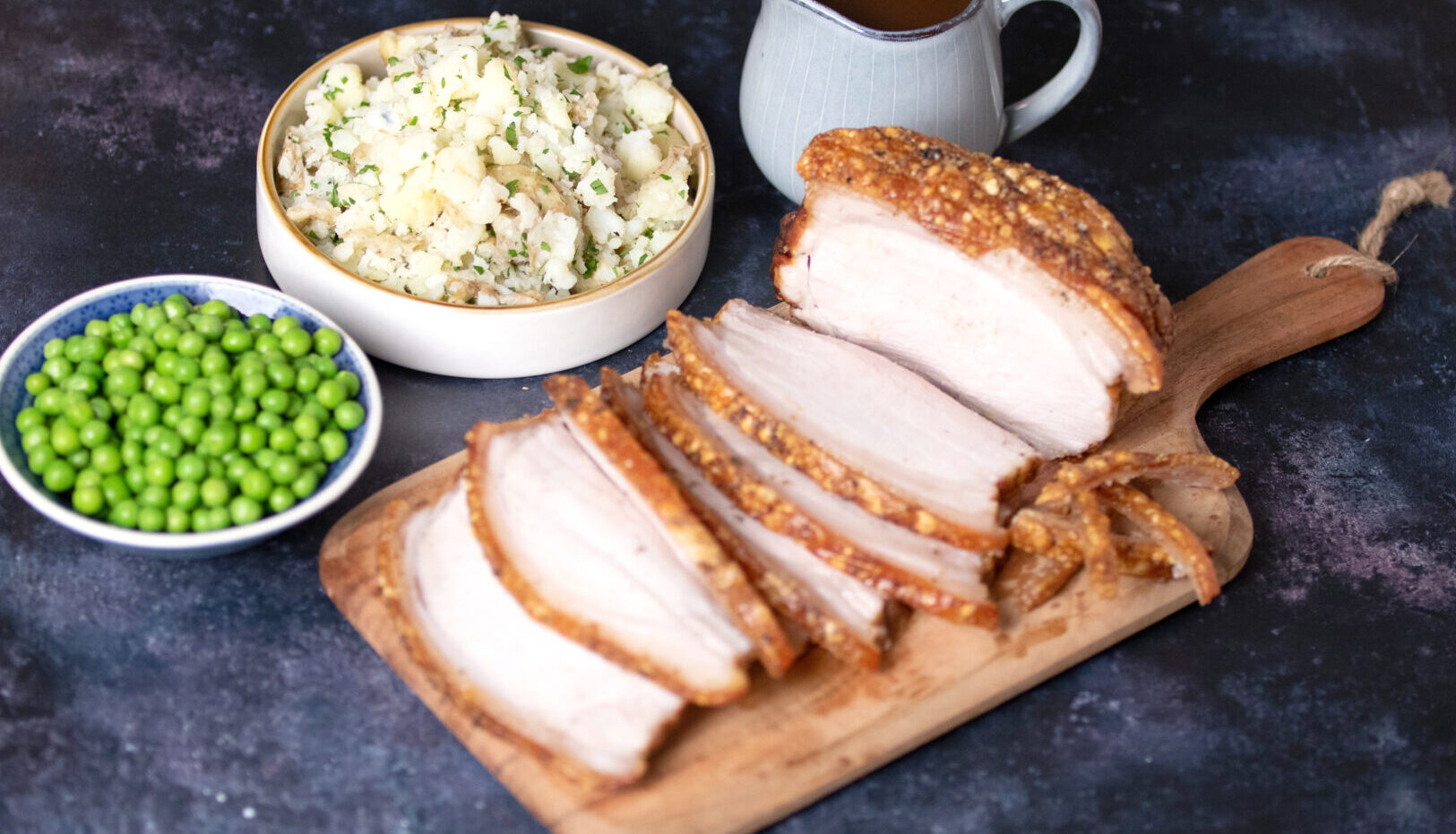 Pork Loin Roast with Crackling, sliced, on a wooden chopping board.
